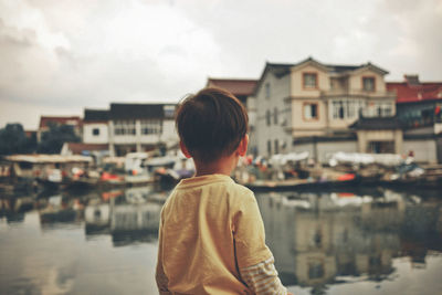 Rear view of boy standing in city against sky