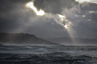 Big waves break on the coast, in the sunlit sea, passing through the clouds. galicia, spain.