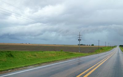 Road by electricity pylon against sky