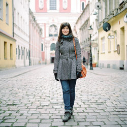 Portrait of woman in warm clothing standing on cobbled street in city