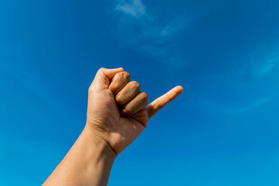 Cropped hand gesturing against blue sky