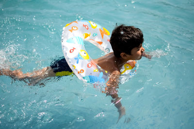 Happy indian boy swimming in a pool, kid wearing swimming costume along with air tube during day