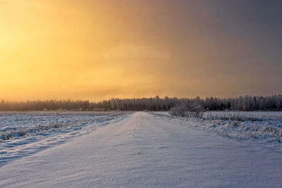 Snow covered field against sky during sunset