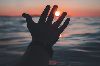 Silhouette hand against sea during sunset