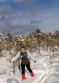 The swamp, a woman rejoices and enjoys walking in snowshoes, snow-covered pines in the background