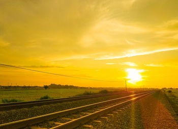 Railroad tracks on field against romantic sky at sunset