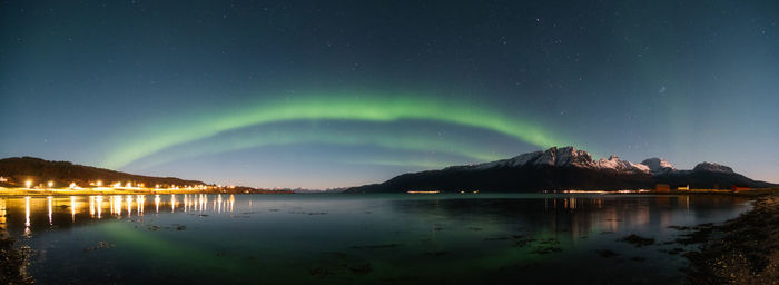 Panoramic view of shoreline with snowcapped mountains against arching northern lights