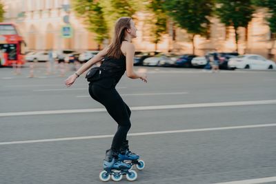 Full length of woman skateboarding on road in city