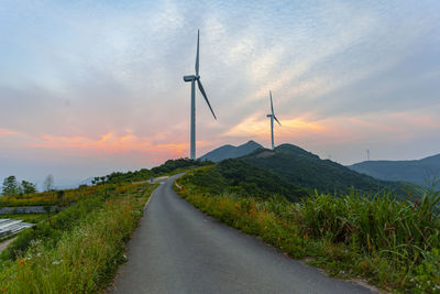 Wind turbines on road against sky during sunset