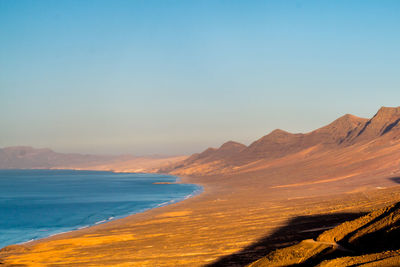 Scenic view of sea and mountains against clear blue sky