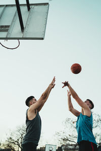 Low angle view of men playing basketball against clear sky