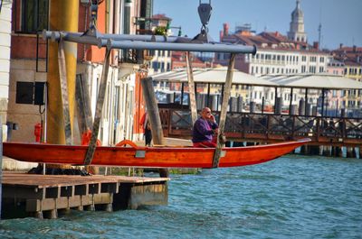 Man sitting on boat in river against buildings