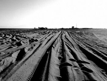 Tire tracks on sandy field against clear sky
