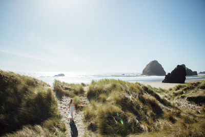 Rear view of young woman walking on trail leading towards beach