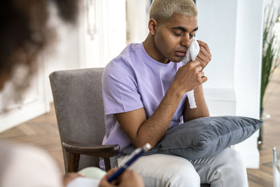 Sad patient sitting in armchair wiping tears with facial tissue