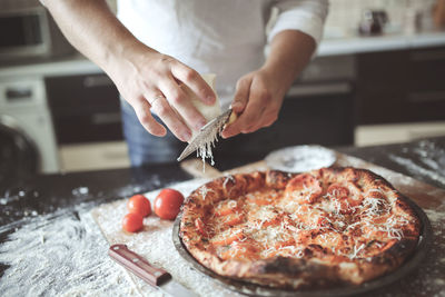 Male hands rubbed cheese grated on pizza, pizza cooking in a real home interior lifestyle and toning