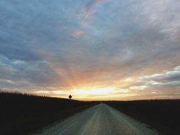 Road passing through field against cloudy sky