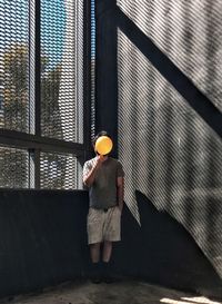 Front view of man holding yellow balloon against windows and wall.