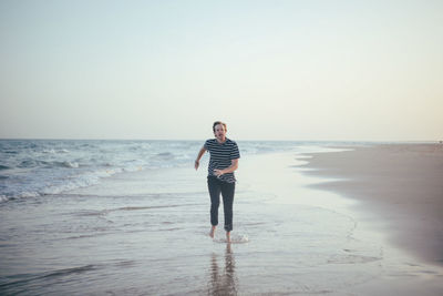 Rear view of woman standing at beach against clear sky
