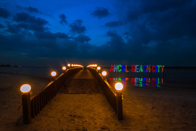 Illuminated lights on beach against sky at night