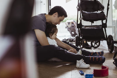 Father tying shoelace of son at home