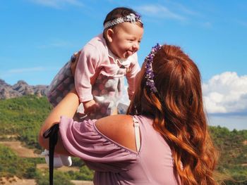 Close-up of mother holding happy daughter against blue sky