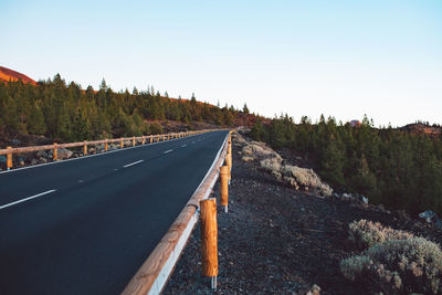 Road leading towards forest against clear sky