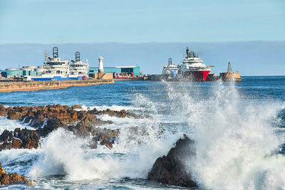 Sea waves splashing on rock formations against sky