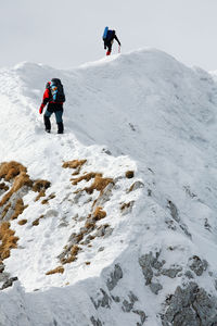 Low angle view of mountaineers climbing snowcapped mountain against sky