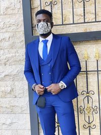 A handsome  young man donning a 3 piece suit and masked up.