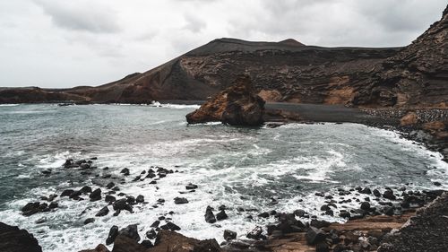 Scenic view of sea by mountain against sky