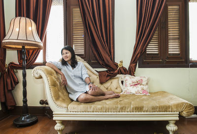 Full length of smiling beautiful woman resting on chaise longue at home