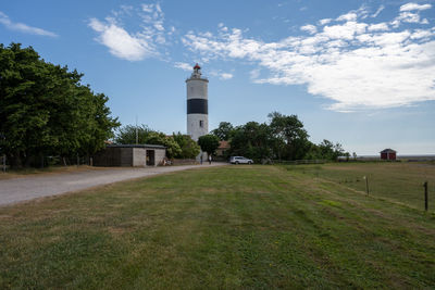 Lighthouse on field by building against sky