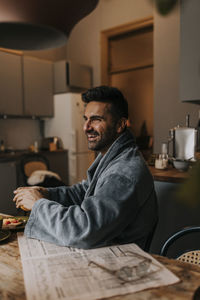 Happy man wearing bathrobe while sitting at dining table in home