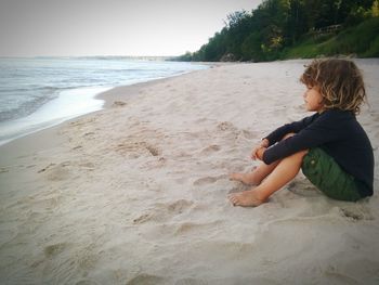 Boy sitting on beach against sky