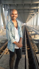 Portrait of a smiling young man standing on rail bridge train is coming. 