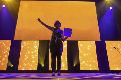 Full length of woman standing against illuminated lighting equipment