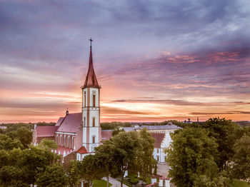 Tower amidst trees and buildings against sky during sunset