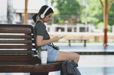 European girl waiting for a train to go on a trip, wearing headphones to music from a smartphone app