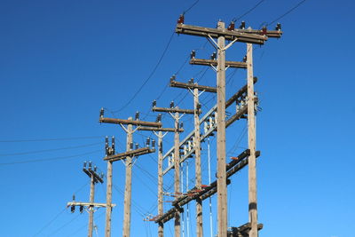 Low angle view of electricity pylon against clear blue sky