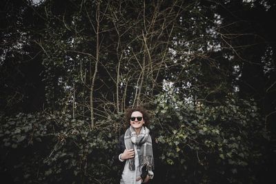 Portrait of young woman standing against trees in forest