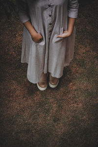 A girl wearing a dress putting her hands inside the pockets standing on the grass 
