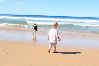 Siblings walking at beach against sky