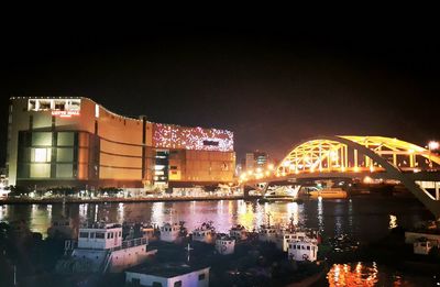 Illuminated buildings by river against sky at night