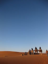 People on sand dune in desert against clear blue sky