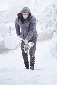 Full length of young man removing snow with shovel on field