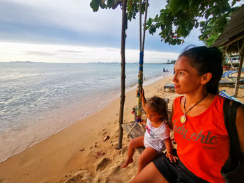 Woman woth baby girl on beach by sea against sky