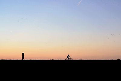 Silhouette men standing on field against sky during sunset