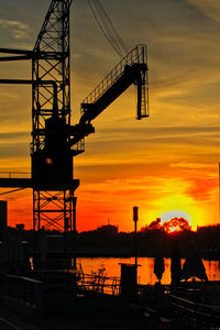Silhouette cranes at construction site during sunset