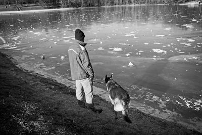 Man with dog standing at frozen lakeshore